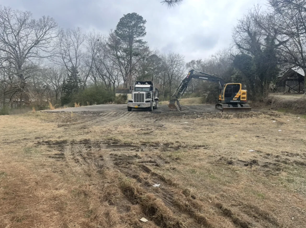 Dump truck and tracked excavator on a scraped-clean pad after a teardown, tire ruts across the lot in the foreground, on a Hot Springs area job