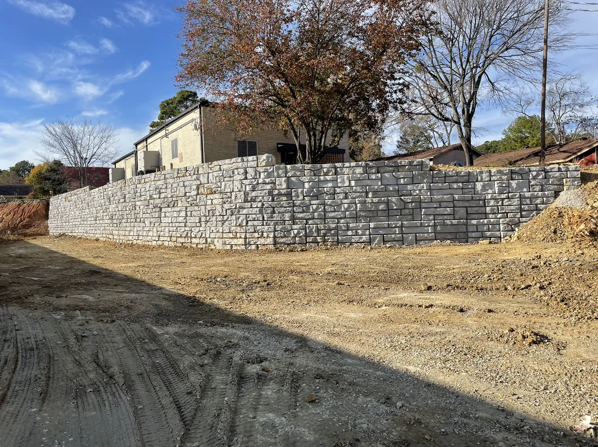 Long segmental block retaining wall holding a slope above a graded gravel pad near Hot Springs