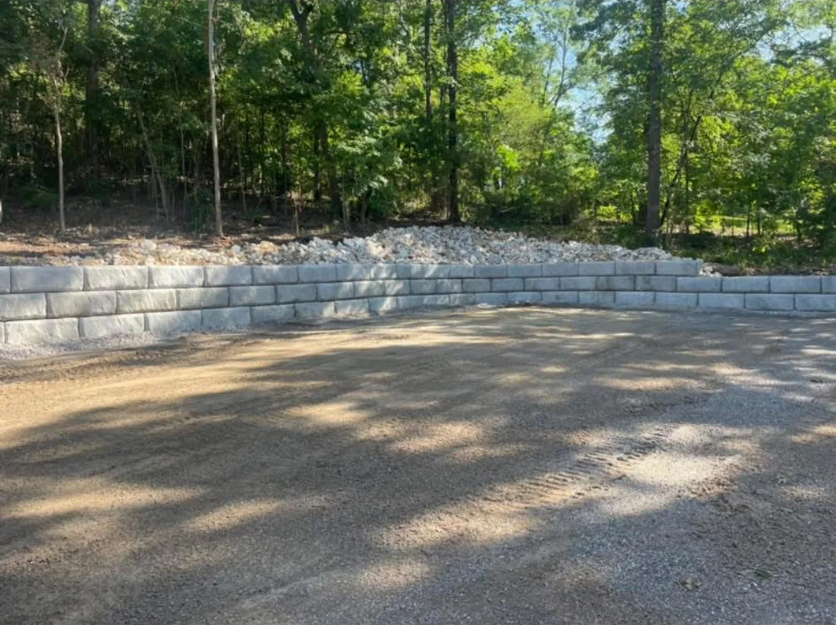Freshly graded gravel pad below a new block retaining wall on a Hot Springs area job