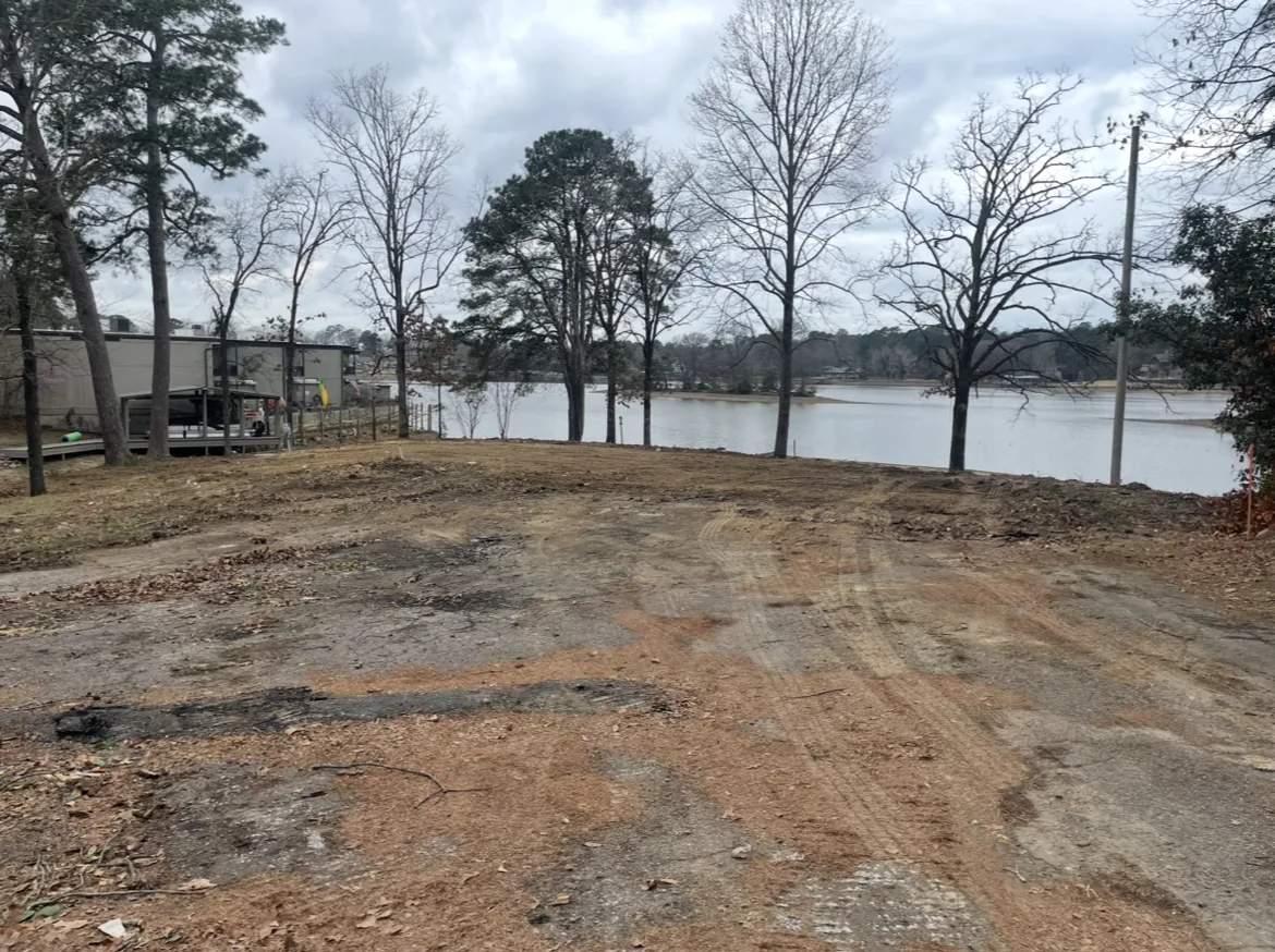 Freshly cleared and graded lakefront lot with bare winter trees, a boathouse and the lake behind it on a Hot Springs area job